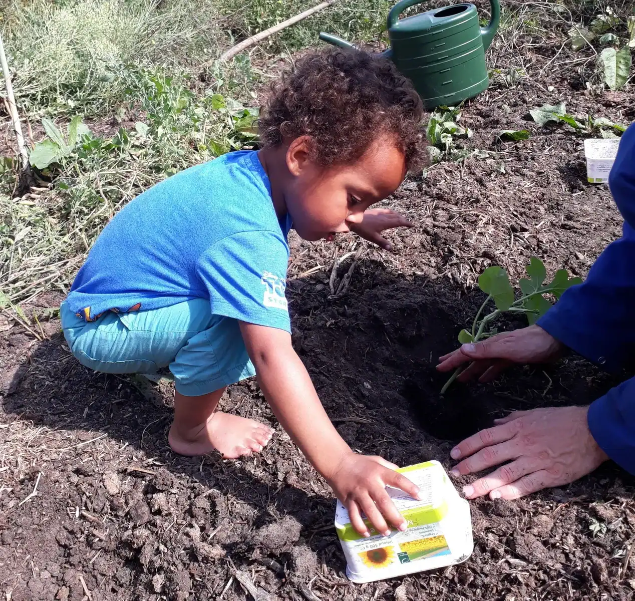 Jouw dagbesteding, jouw nieuwe plek. | Een jong kind en een volwassene die samen een klein plantje in de tuinbedden van De Junahoeve planten. | Samen tuinieren.